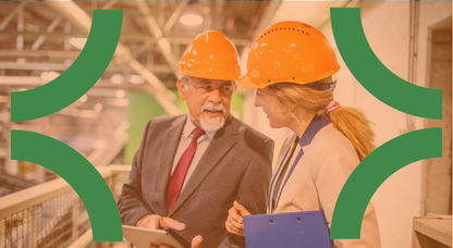Man and woman in har hats and suits standing looking over a factory floor